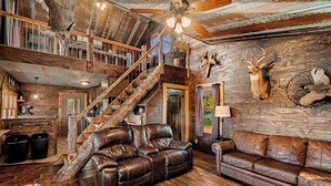 A rustic cabin interior with a wooden staircase, leather sofas, and mounted animal heads on the walls. - Cabin on Private 4-Acre Pond, King Bed (Junction City)
