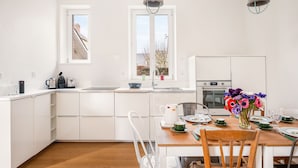 A modern kitchen with white cabinetry, a wooden dining table set for four, and a vase of flowers on the table.