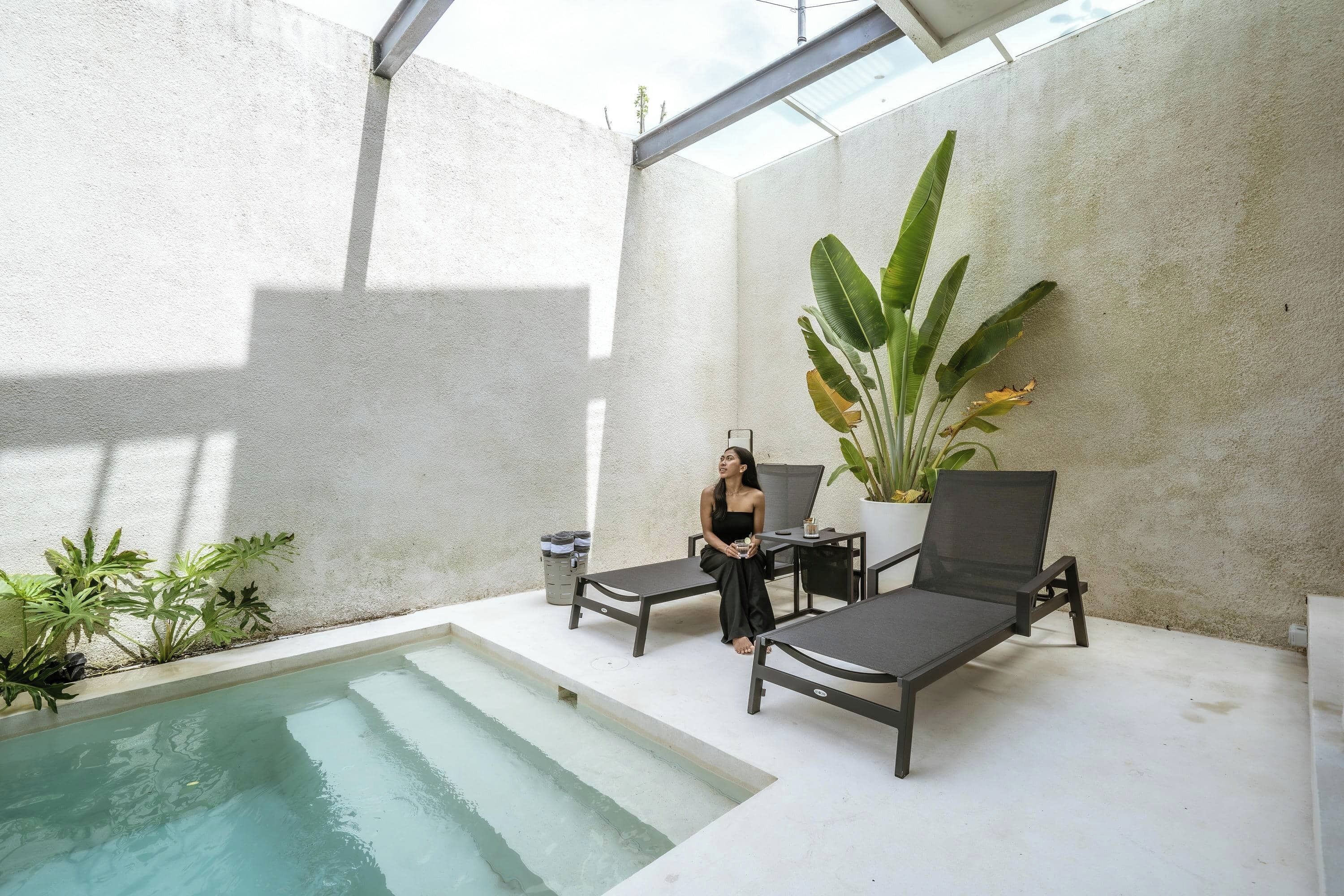 A poolside area with a seating arrangement, a potted plant, and a concrete wall.