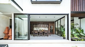 A modern house with a glass door leading to a dining area with a kitchen in the background. - Villa Sabilla Bingin (Pecatu)