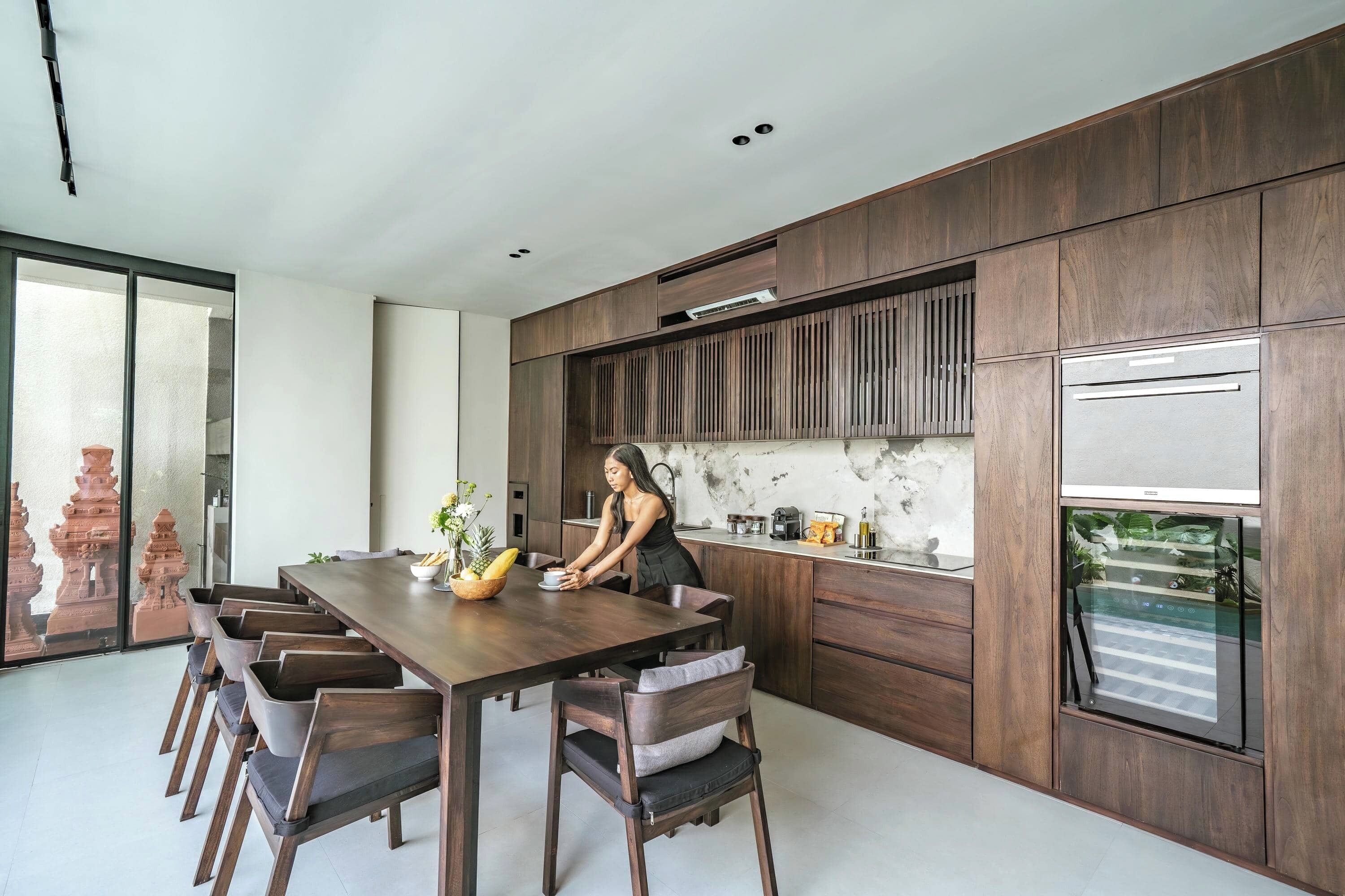 A modern kitchen with wooden cabinetry, a built-in oven, and a dining area with a long table and chairs.