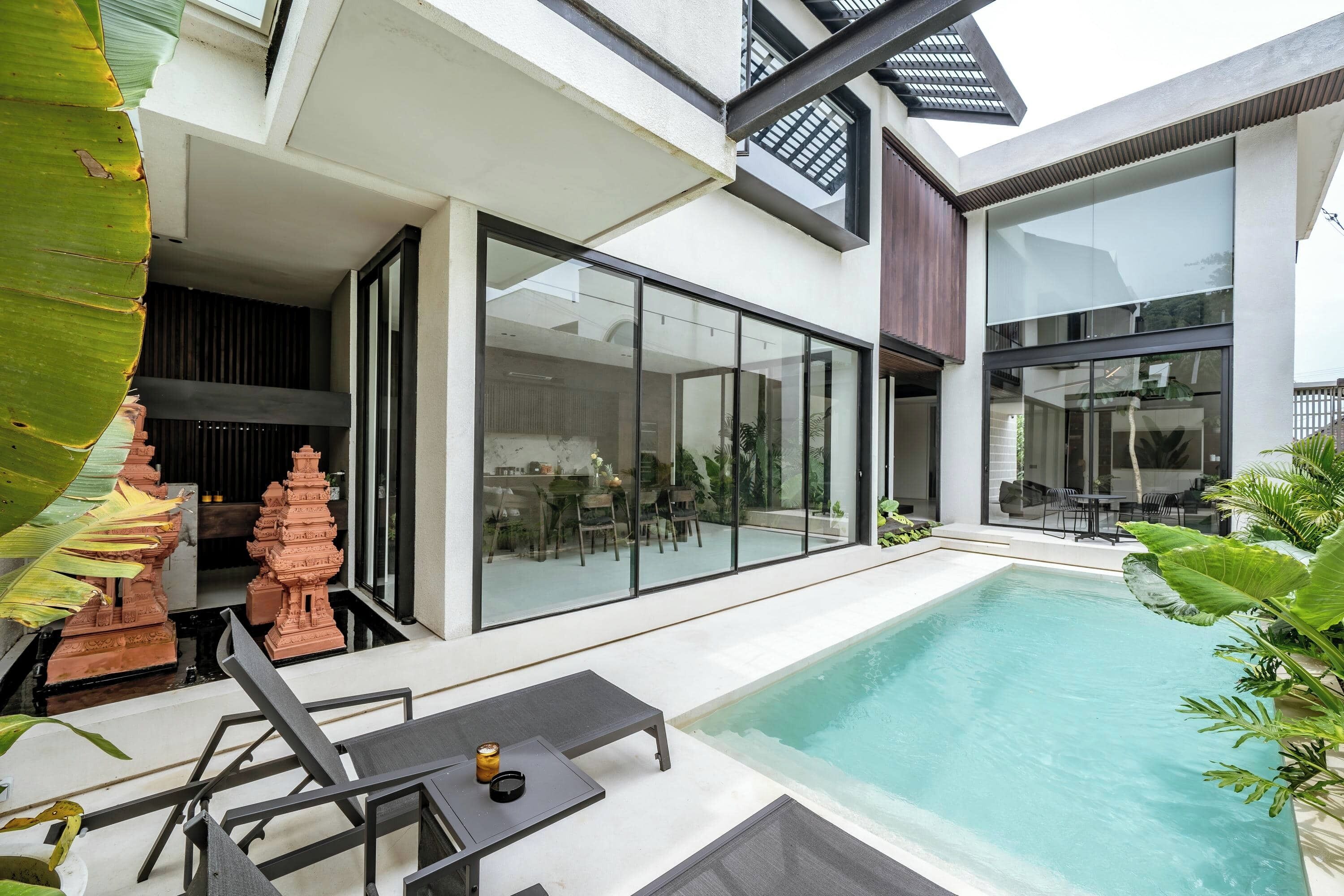 A modern house with a swimming pool, large windows, and a patio area with a table and chairs.