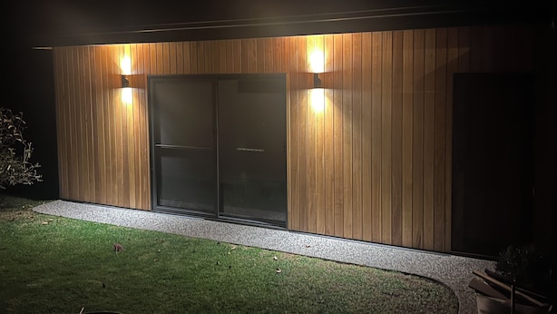 Un edificio moderno con facciata in legno, due ampie porte in vetro e due luci a parete.