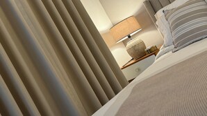 A hotel room with a bed, a bedside table with a lamp, and a window with blinds. - Xuite Home One Bedroom Suite (Punta Cana)