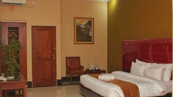A hotel room with a bed, a chair, a small table, a plant, and a door.