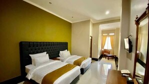A hotel room with two beds, a wooden desk, a chair, and a television. - Rizen Padjadjaran Hotel (Bogor)