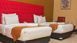 A hotel room with two beds, a red tufted headboard, white bedding, and a painting on the wall. - Rizen Padjadjaran Hotel (Bogor)