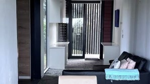 A modern living room with a dining table, a sofa, and a ceiling fan. - Fraser Coast, Eco Container Home + Cabin, Pool, Pet Friendly, Boat Ramp 5min (River Heads)