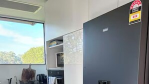 A kitchen with a black refrigerator, white cabinets, and a window with a view of trees. - Fraser Coast, Eco Container Home + Cabin, Pool, Pet Friendly, Boat Ramp 5min (River Heads)