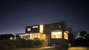 A modern house with large windows and a well-lit interior at night. - Fraser Coast, Eco Container Home + Cabin, Pool, Pet Friendly, Boat Ramp 5min (River Heads)