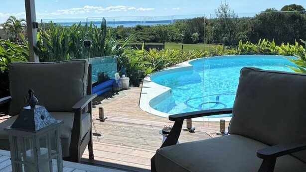 A covered outdoor area with a pool, lounge chairs, and a view of the ocean. - Fraser Coast, Eco Container Home + Cabin, Pool, Pet Friendly, Boat Ramp 5min (River Heads)