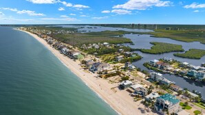 An aerial view of a coastal residential area with houses along the beach, a marina, and a bridge in the background. - Beach Dayz | Walk to Beach, Restaurants, Boat Dock & More (Bonita Springs)