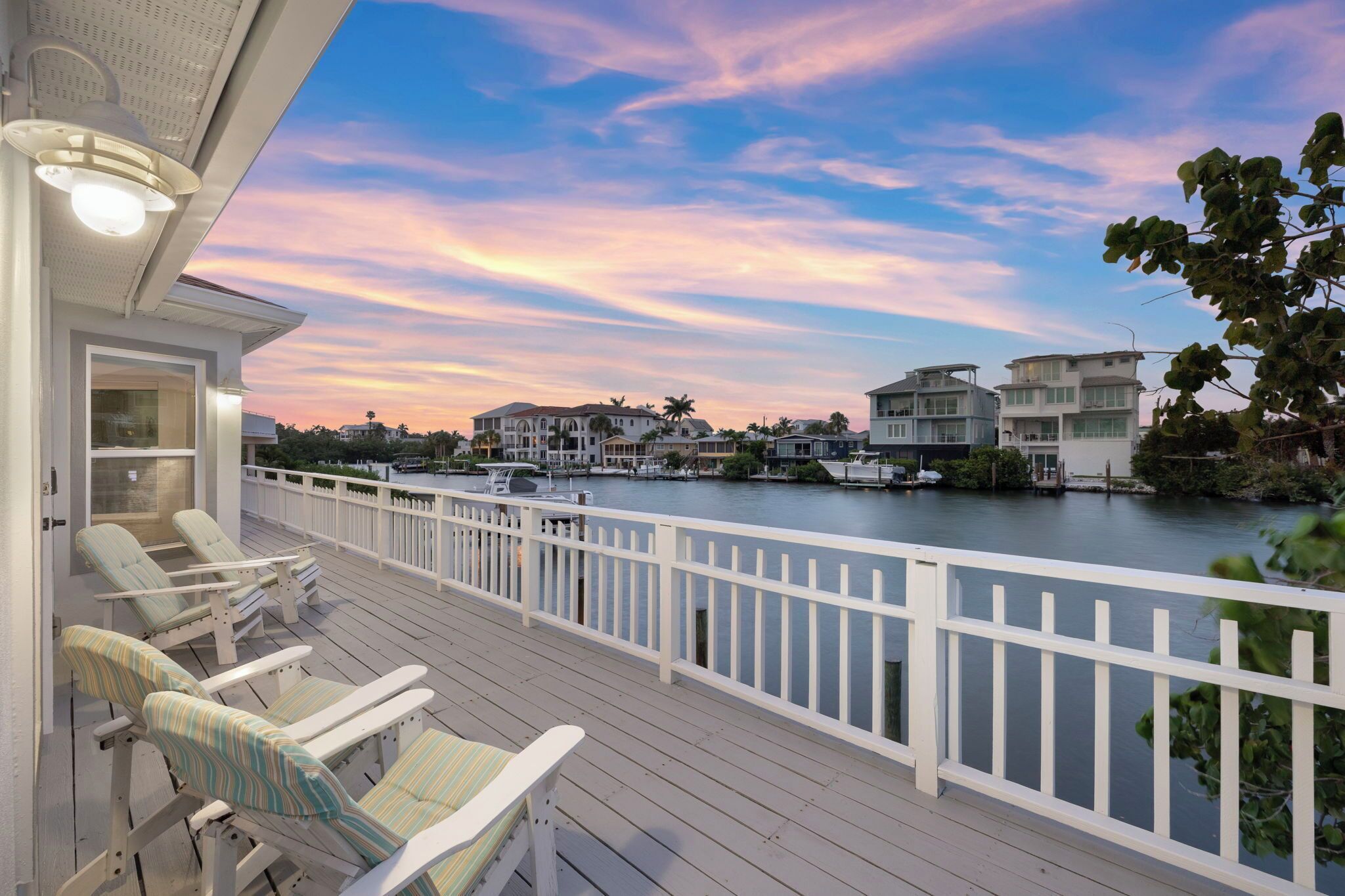A waterfront property with a deck, lounge chairs, and a view of the water and neighboring houses.