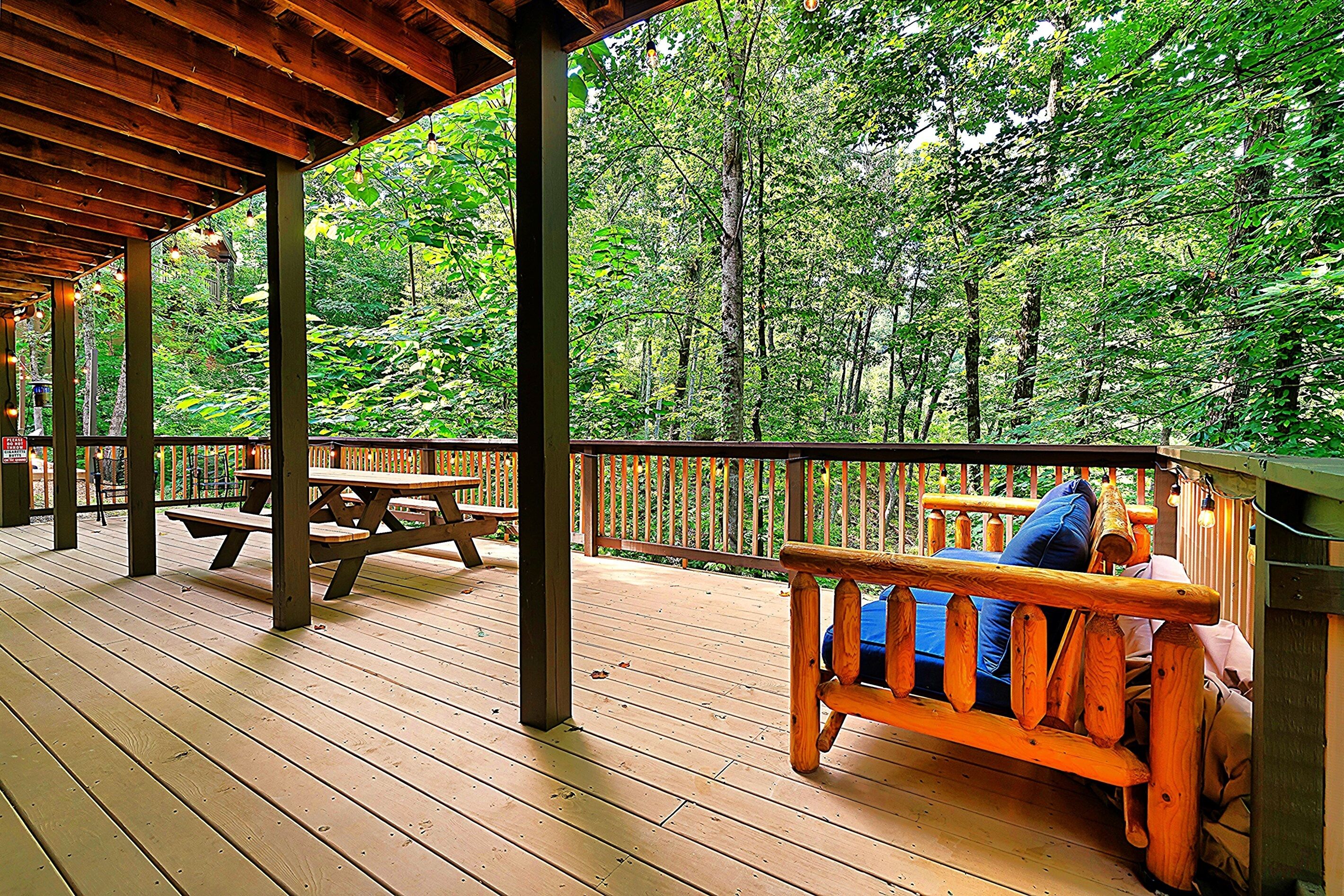 Une terrasse en bois avec des tables de pique-nique et un banc donnant sur une forêt.