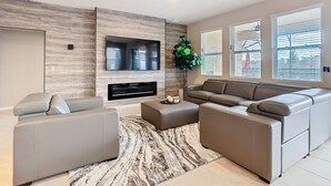 Un salon moderne avec un téléviseur à écran plat, un canapé d’angle, une table basse et une grande plante en pot.