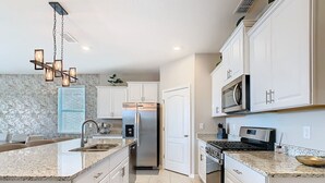 Une cuisine moderne avec des meubles blancs, des appareils en acier inoxydable et des plans de travail en granit.