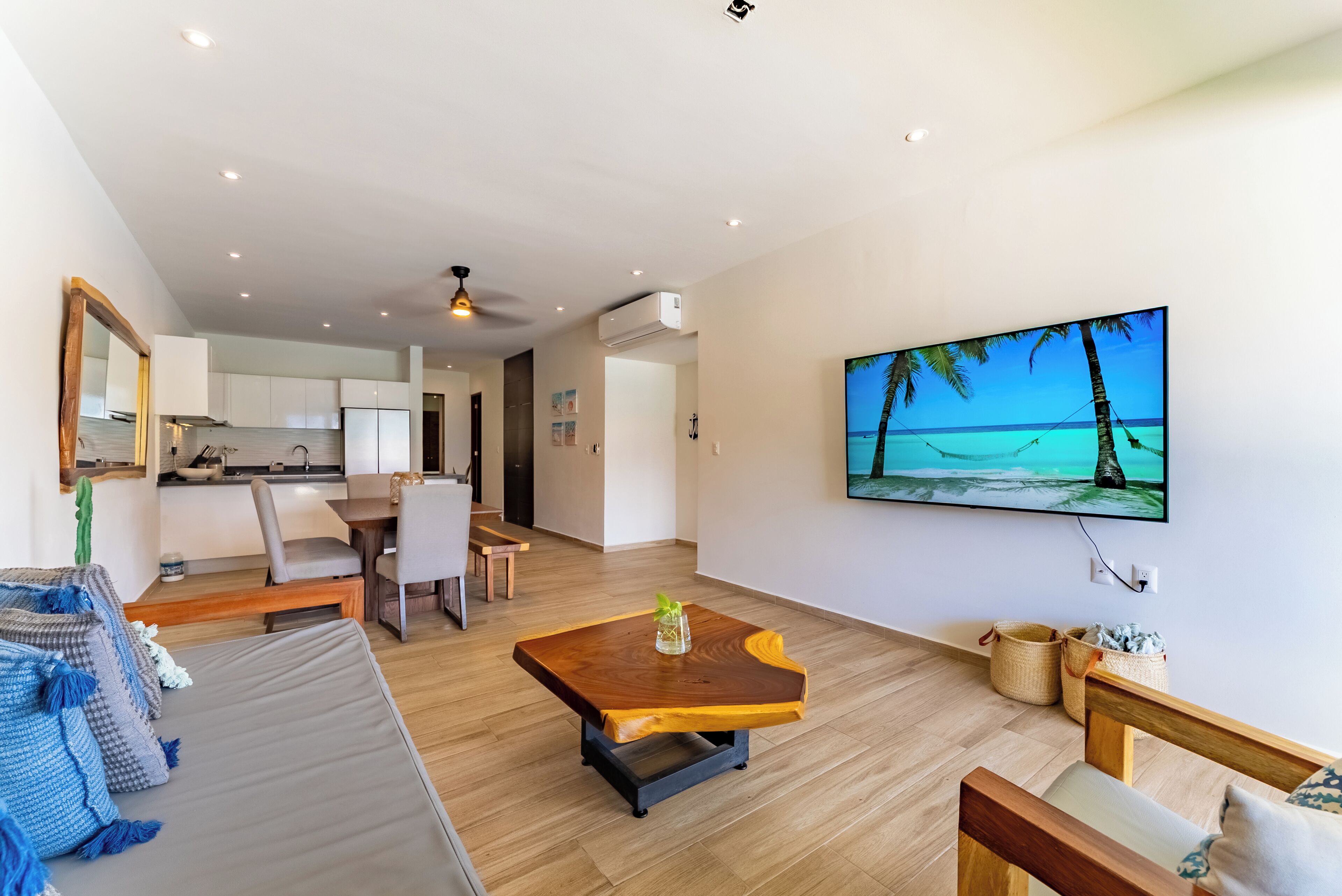 Ein modernes Wohnzimmer mit Couch, Fernseher und Couchtisch aus Holz. Auf dem Fernseher ist eine Strandansicht zu sehen.