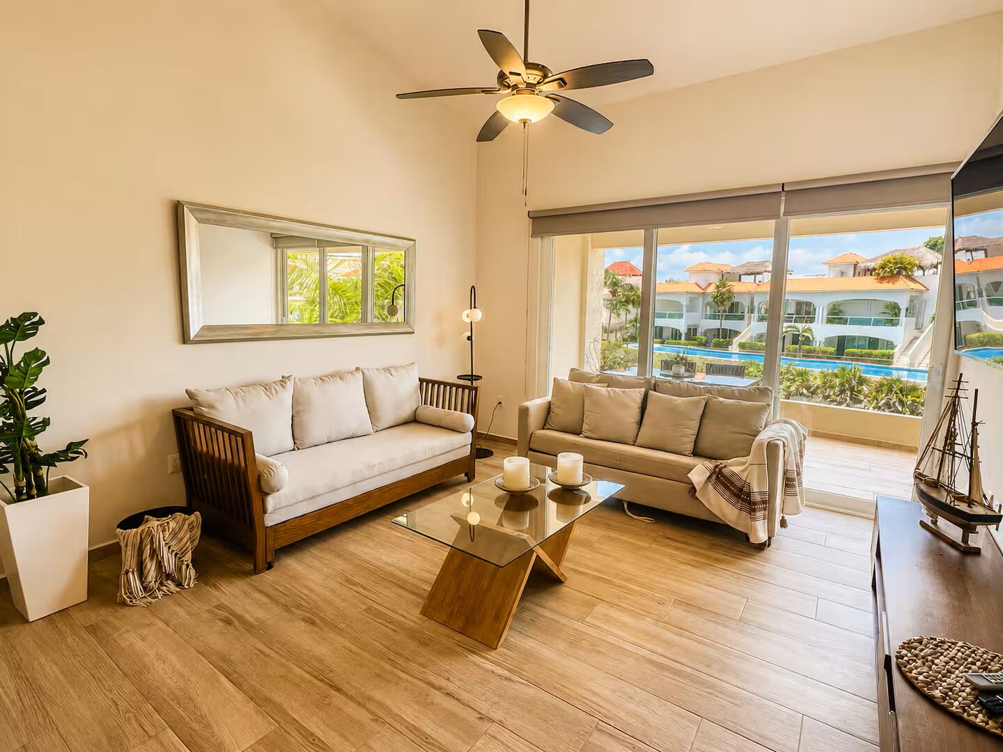 A spacious living room with a ceiling fan, two sofas, a coffee table, and a large window offering a view of a pool and buildings.