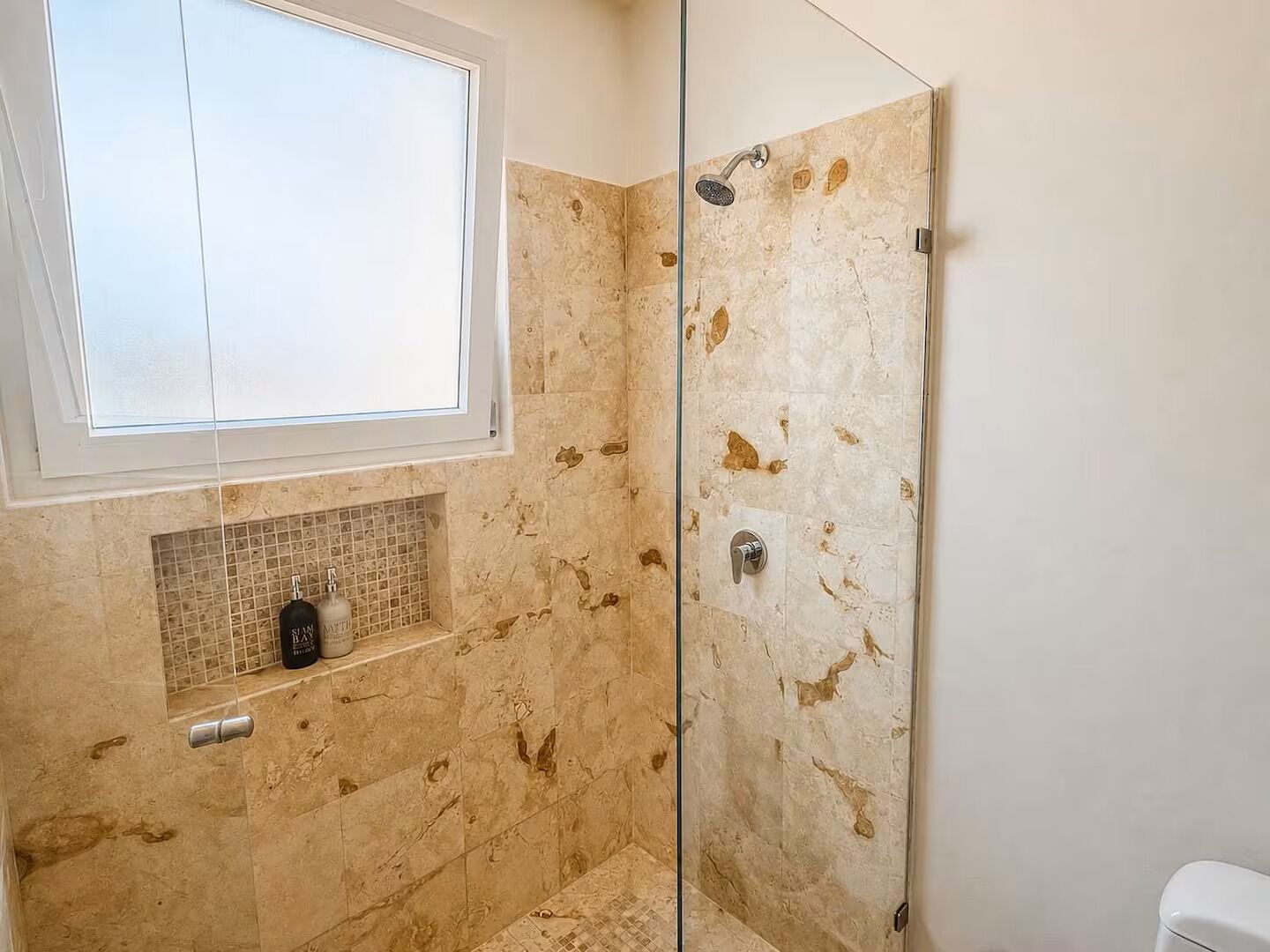 A bathroom with a glass shower enclosure, a window above the sink, and a tiled backsplash.