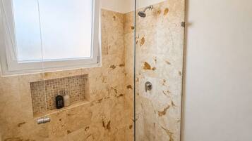 A bathroom with a glass shower enclosure, a window above the sink, and a tiled backsplash.