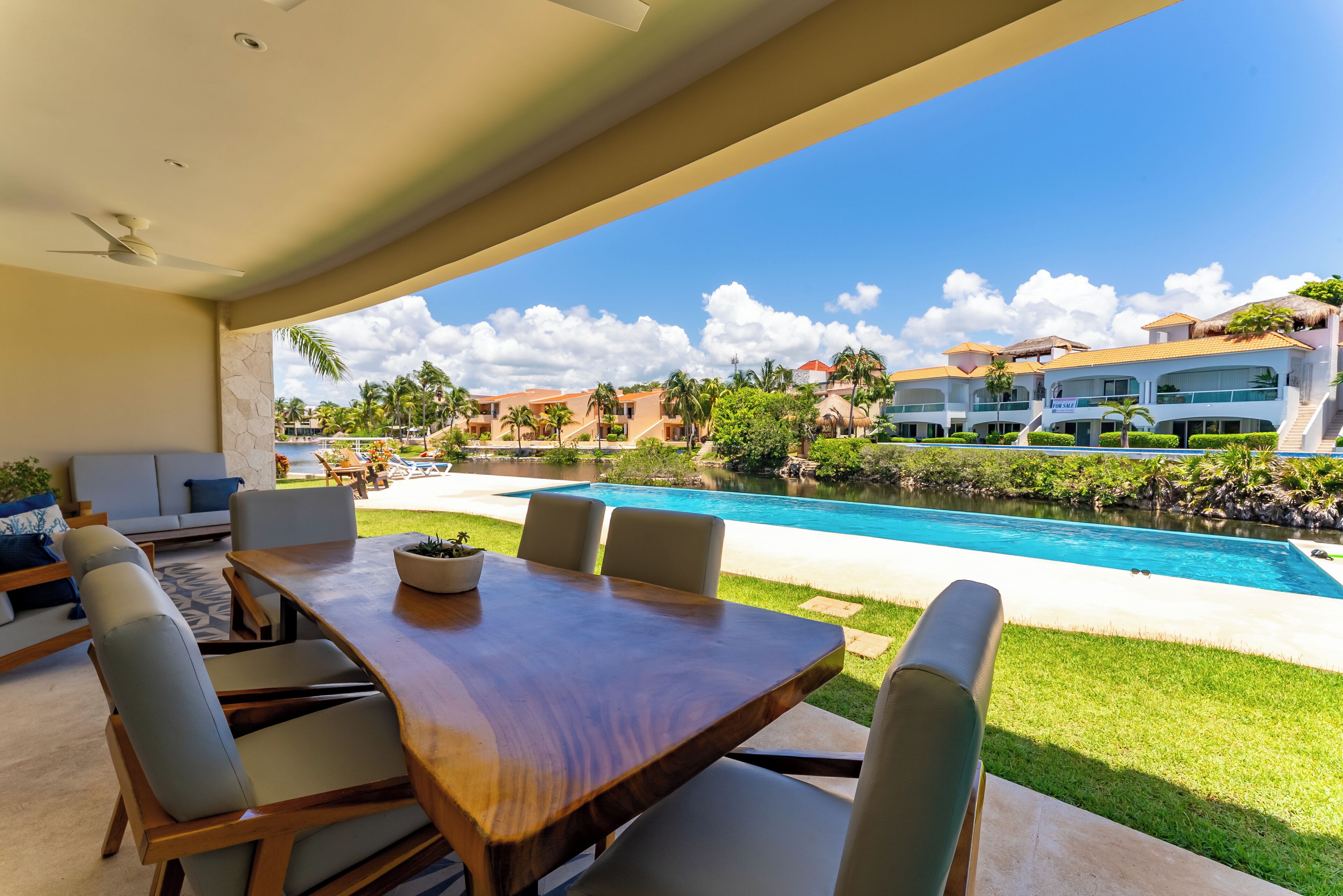 Un comedor con mesa y sillas de madera, un sofá y vistas a una piscina y edificios de un complejo turístico.