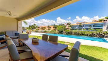 Un comedor con mesa y sillas de madera, un sofá y vistas a una piscina y edificios de un complejo turístico.