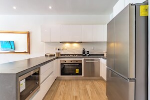 A modern kitchen with stainless steel appliances, wooden flooring, and white cabinetry.