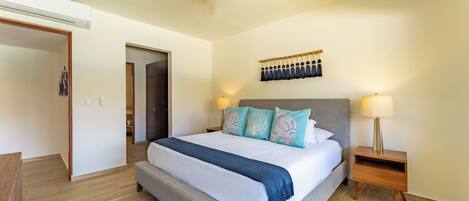 A spacious bedroom with a large bed, a ceiling fan, a nightstand with a lamp, and a wooden floor.