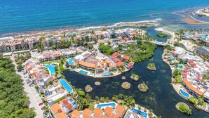 Vista aérea de um resort costeiro com vários edifícios, piscinas e um porto de iates.