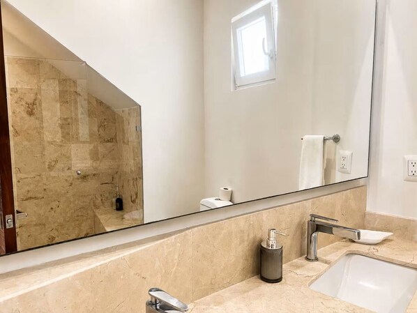 Et badeværelse med et stort spejl, en vask, et toilet og en bruseniche.