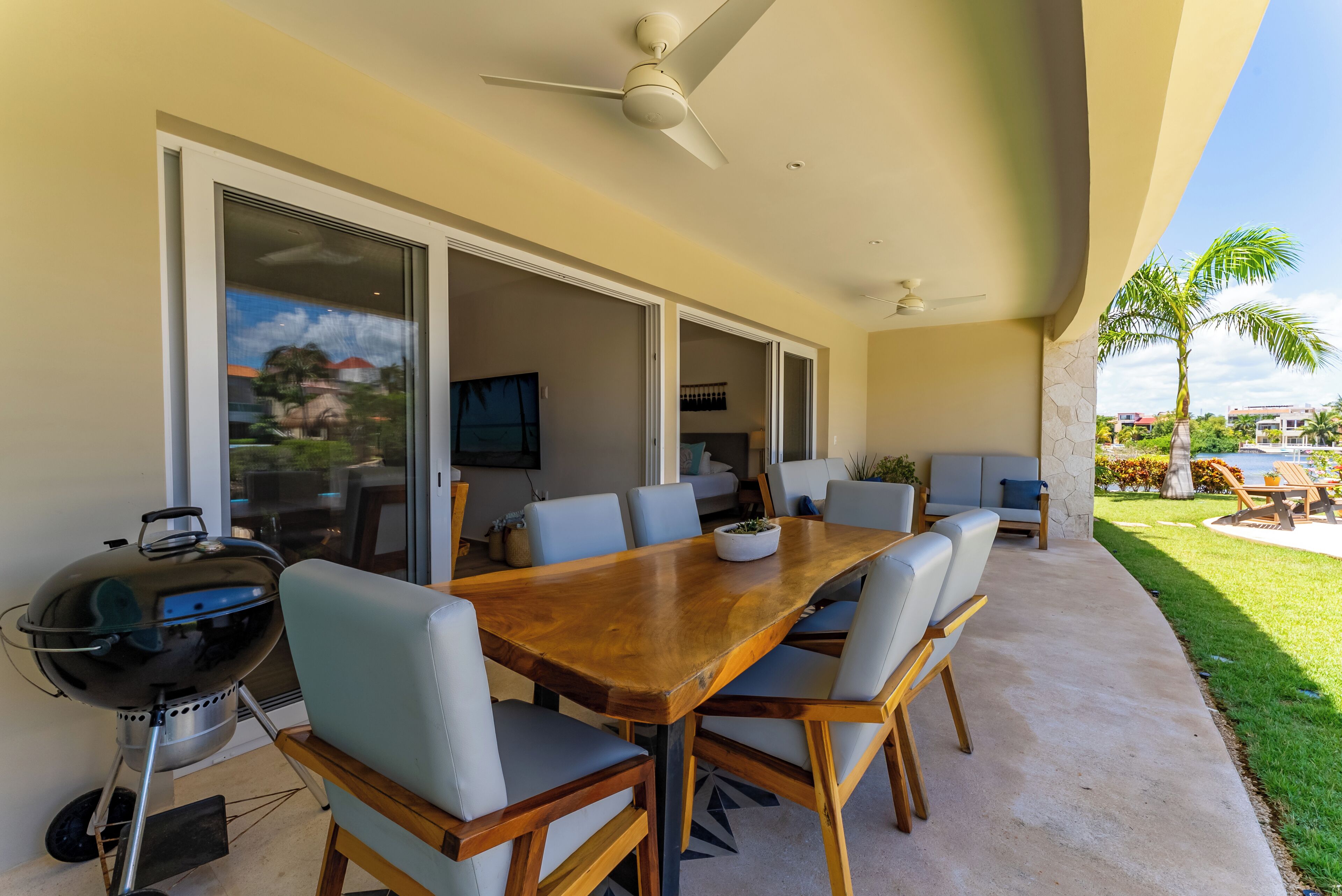 Un espacio de comedor al aire libre con una mesa y sillas de madera, una parrilla y una pantalla de televisión.