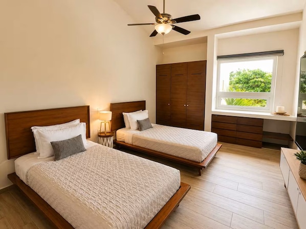 A hotel room with two beds, a ceiling fan, a window with a view of greenery, and a TV on a wooden cabinet. - Lagoon Front Infinity Pool Paddleboard And Fun Puerto Aventuras (Puerto Aventuras)
