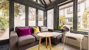 A conservatory with a grey sofa, a round table, and a white chair. - Robin`s Nest, 1 bedroom near Wimbledon (London)