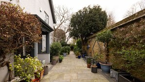 A narrow pathway flanked by potted plants and a building with a white facade. - Robin`s Nest, 1 bedroom near Wimbledon (London)