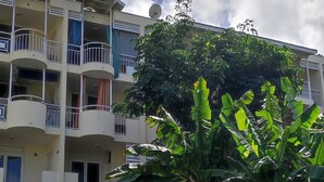 A multi-story residential building with balconies, a satellite dish, and a well-maintained lawn with banana plants. - Studio Voile au vent (La Trinité)
