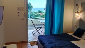 A bedroom with a bed, a desk, and a view of the outdoors. - Studio Voile au vent (La Trinité)