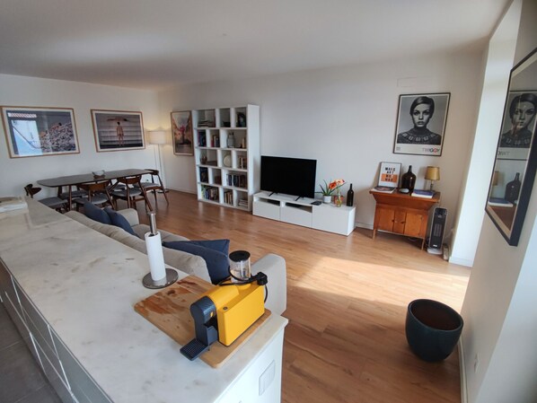 A modern living room with a sofa, TV, bookshelf, and a dining area.