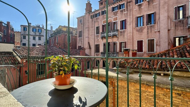 A balcony with a potted plant, a round table, and a view of historic buildings with red-tiled roofs.