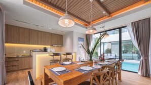 Une cuisine moderne avec des meubles en bois, un coin repas avec une table et des chaises en bois, et une grande fenêtre donnant sur une piscine.