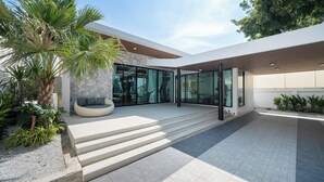 Un bâtiment moderne avec une façade en pierre, de grandes fenêtres en verre et un palmier au premier plan.