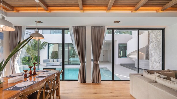 Un espace repas moderne avec une table en bois, des chaises et une vue sur une piscine, visible à travers de grandes portes vitrées.