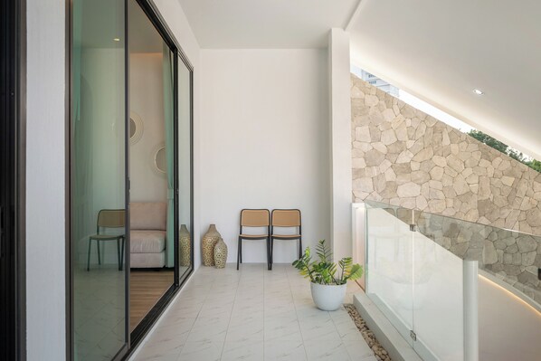 A modern interior with a glass door leading to a seating area, a stone wall, and a potted plant. - Mövenpick Pool Villa 6BR (Sattahip)