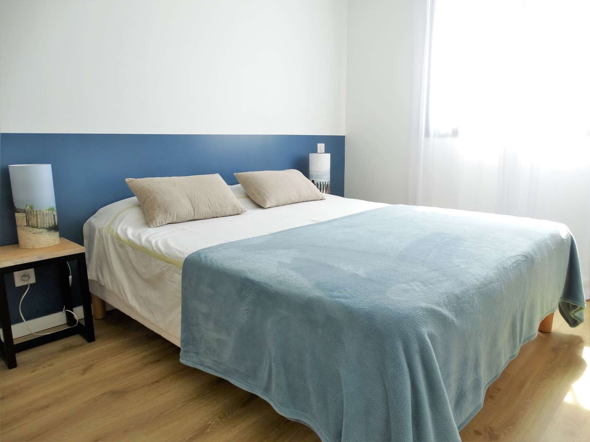 A neatly made bed with a blue blanket, a bedside lamp, and a small table with a lamp.
