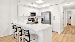 A modern kitchen with white cabinetry, a stainless steel refrigerator, a microwave, and a large island with bar stools.