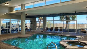 An indoor swimming pool with clear blue water, surrounded by lounge chairs and exercise equipment.