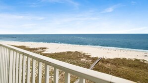 A beach view from a balcony with a railing, ocean, and sandy shore.