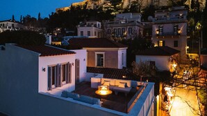 A rooftop terrace with a fire pit, overlooking a historic cityscape with a prominent hill and ancient ruins.
