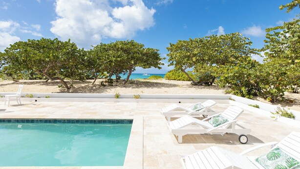 A poolside area with lounge chairs and a view of the beach and ocean.