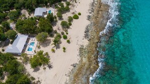 An aerial view of a coastal property with two buildings, a swimming pool, and a beach.
