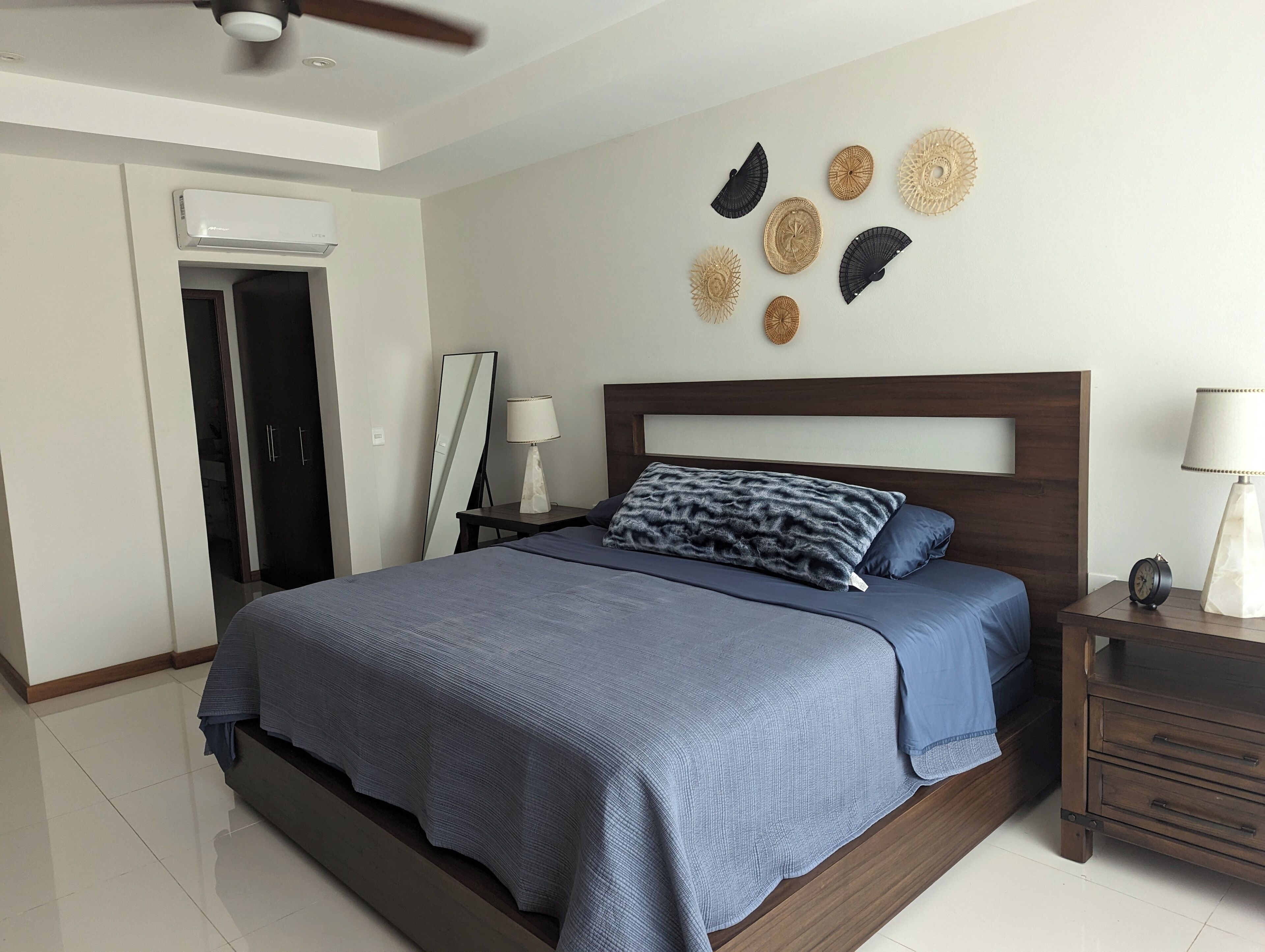 Een moderne slaapkamer met een groot bed, een nachtkastje, een spiegel en decoratieve wanddecoratie.